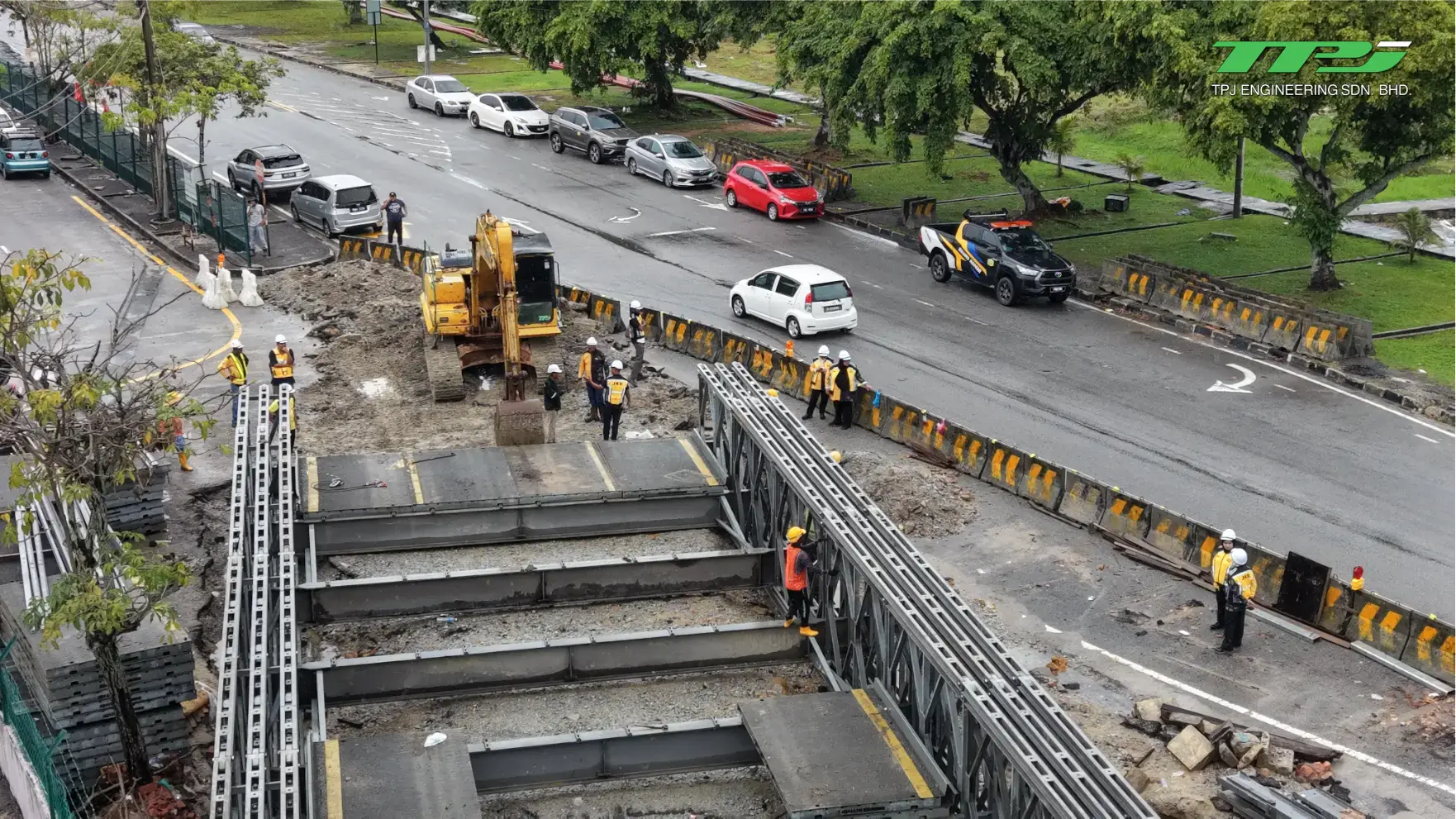 Aerial view of workers installing bridge deck sections beside active traffic at the Carrefour Bridge site.