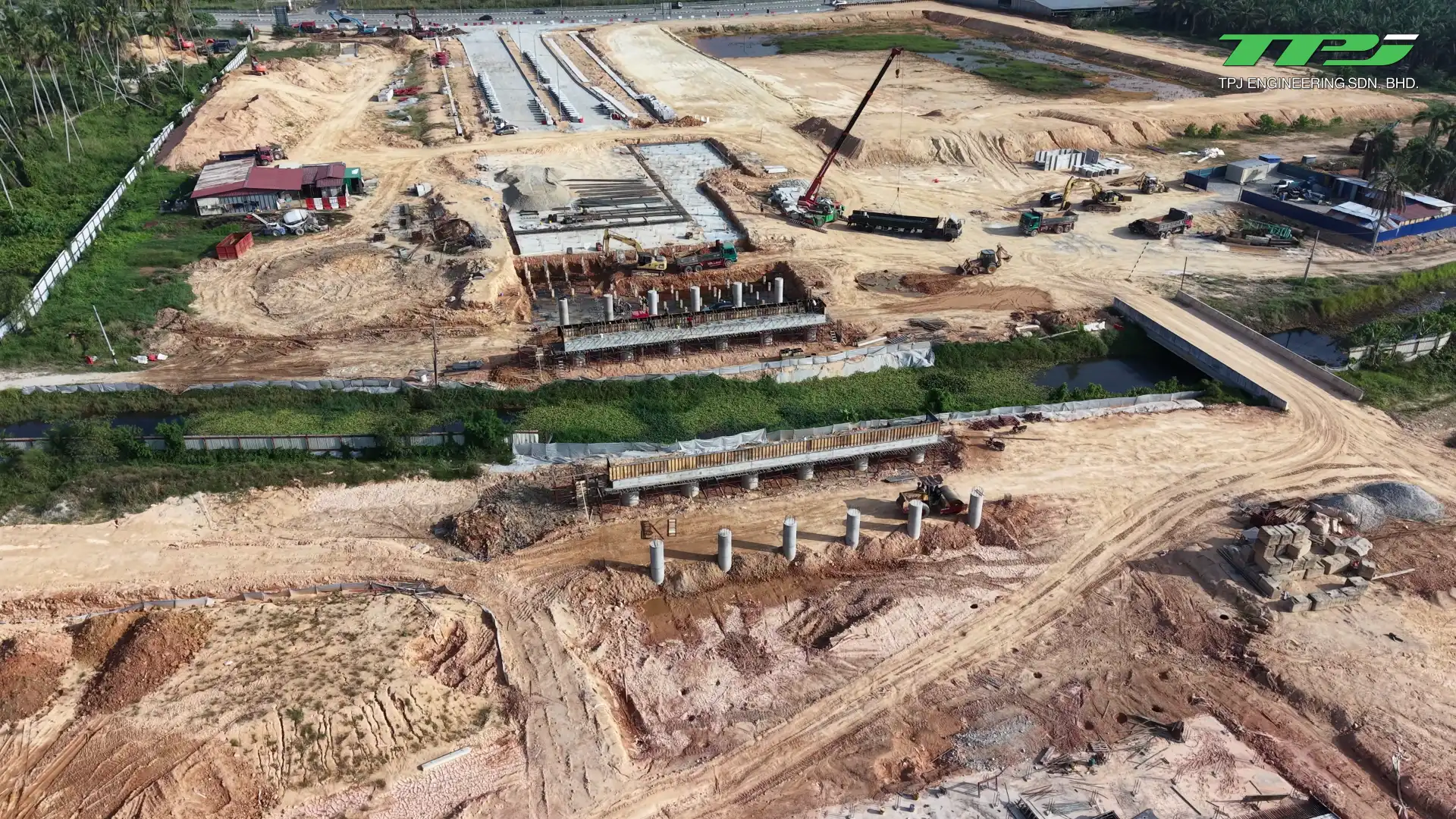 Wide aerial view of bridge foundations, earthworks and a crane beside Sungai Binjai at Batu Kawan, Penang.