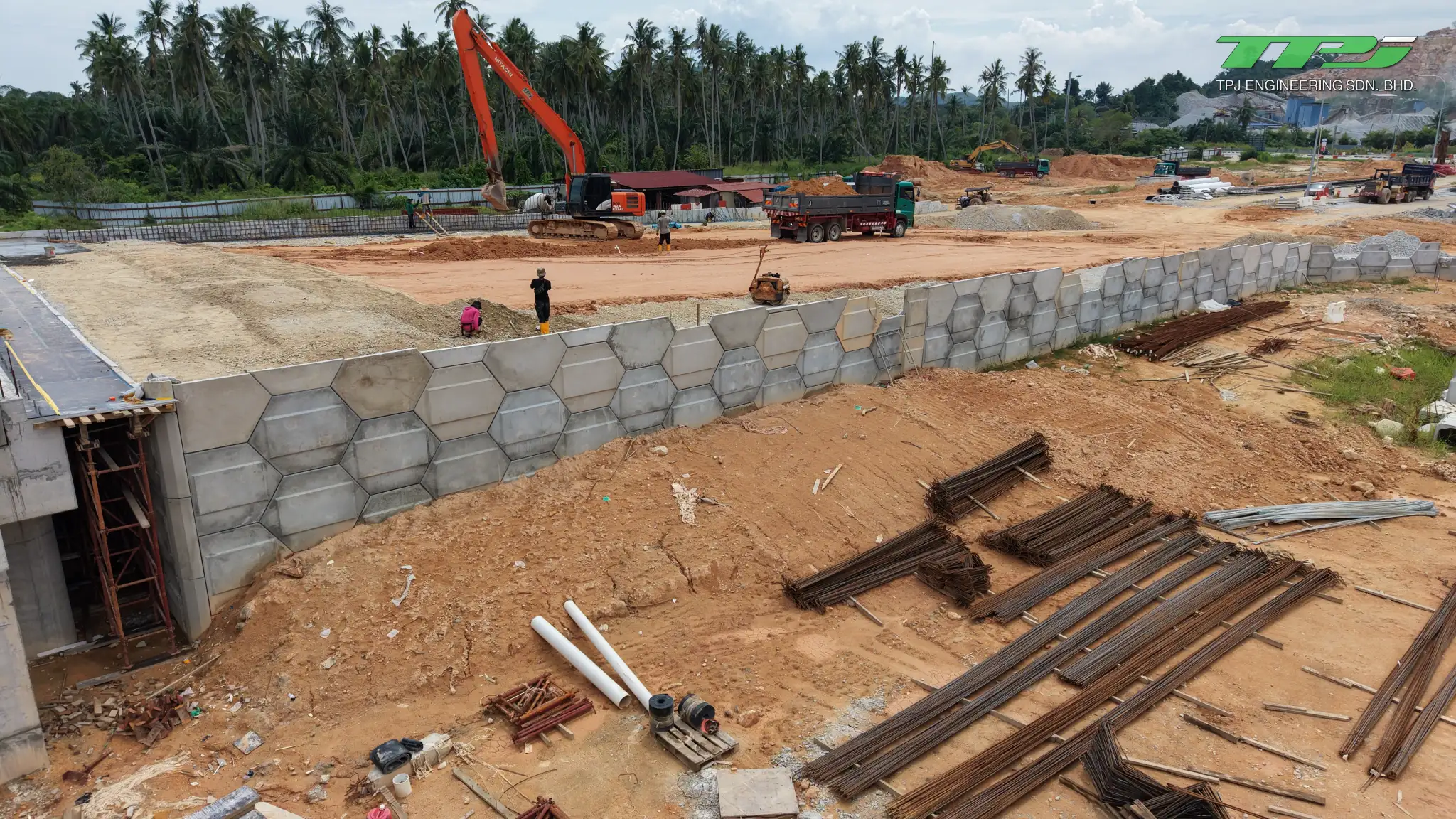 Hexagonal concrete retaining wall at the Batu Kawan bridge site, with reinforcement and an excavator nearby.