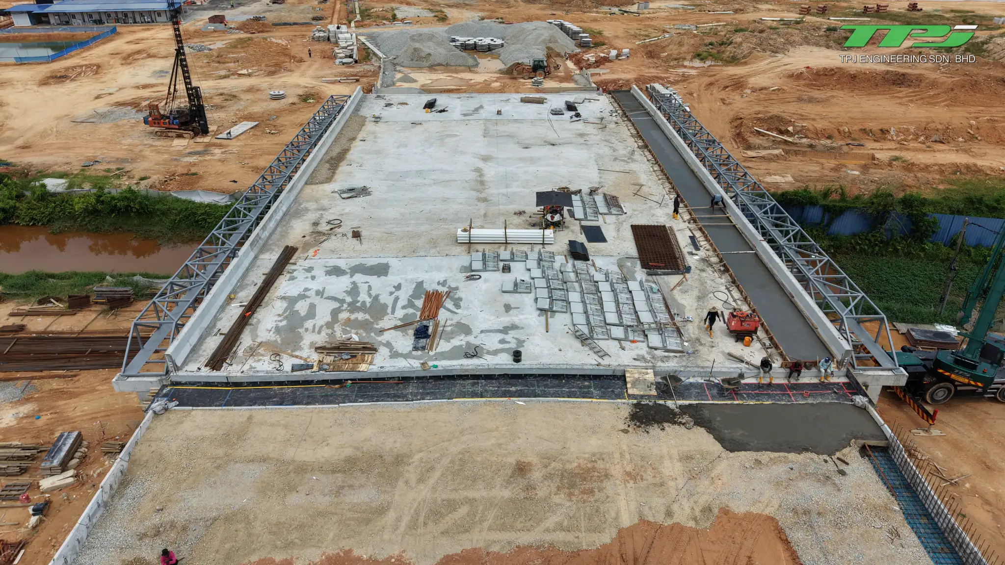 Overhead view of the Batu Kawan bridge deck with stacked materials and workers along the edge.