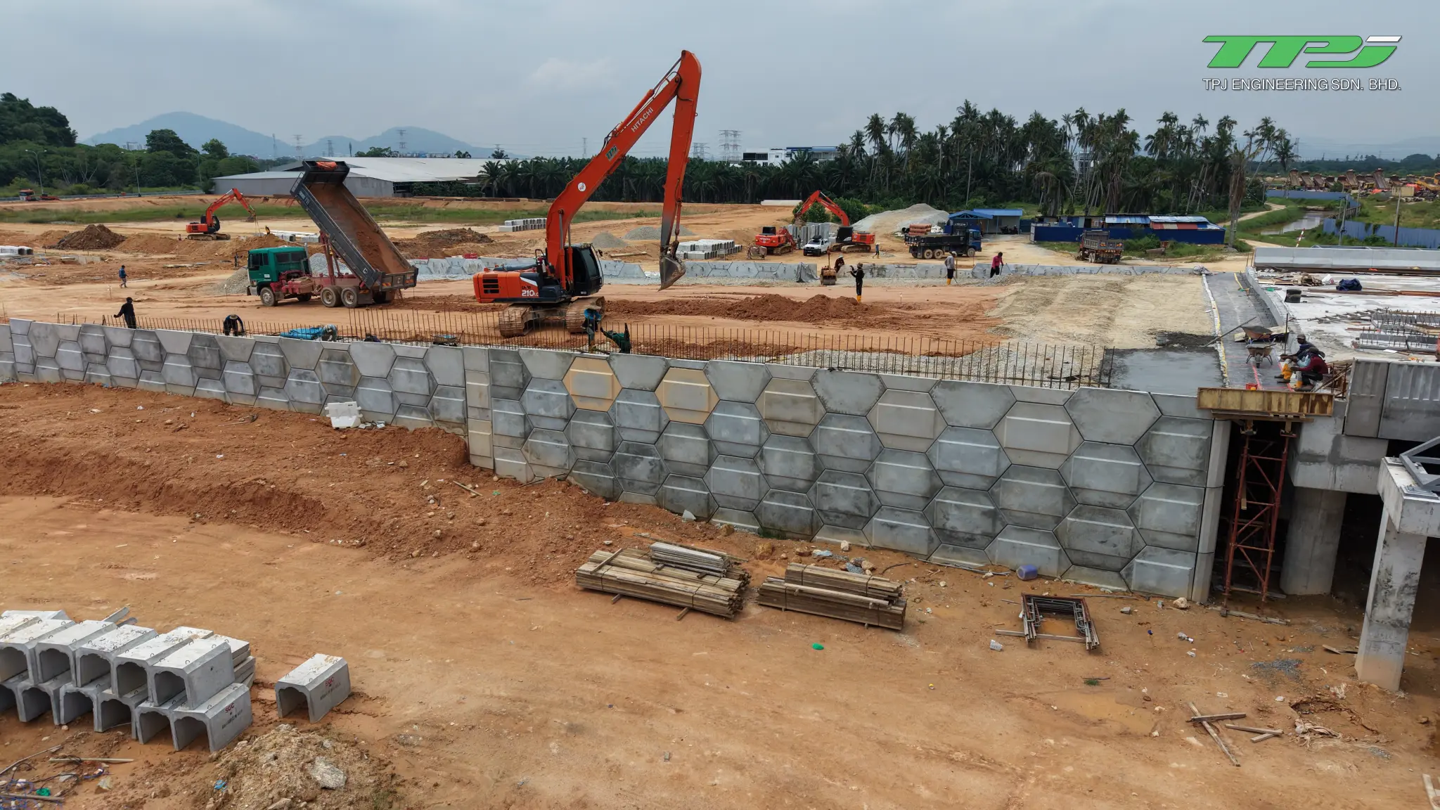 Concrete retaining wall beside the Batu Kawan bridge abutment, with workers, an excavator and a tipper lorry.