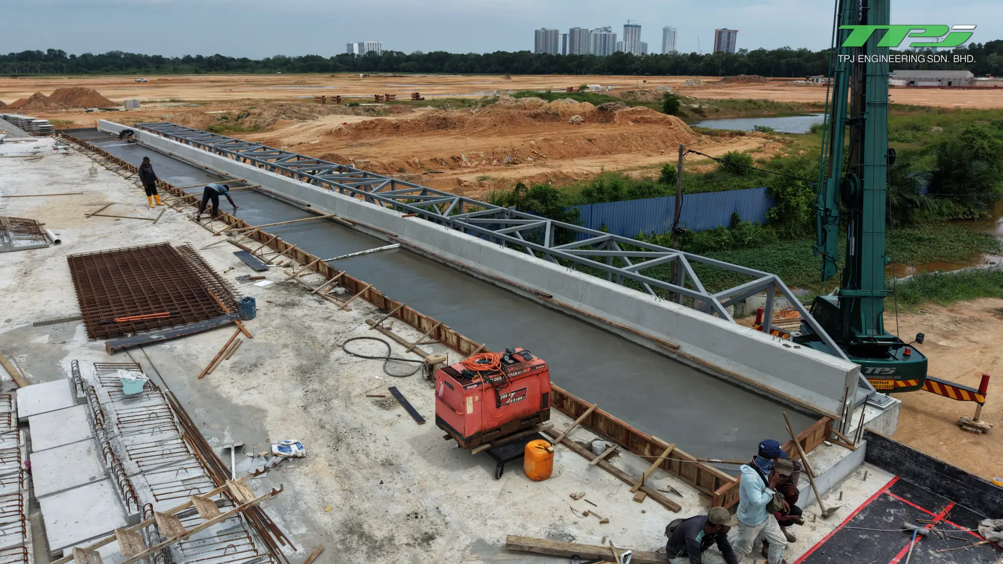 Workers beside concrete edge works and formwork on the Batu Kawan bridge deck, with a crane alongside.