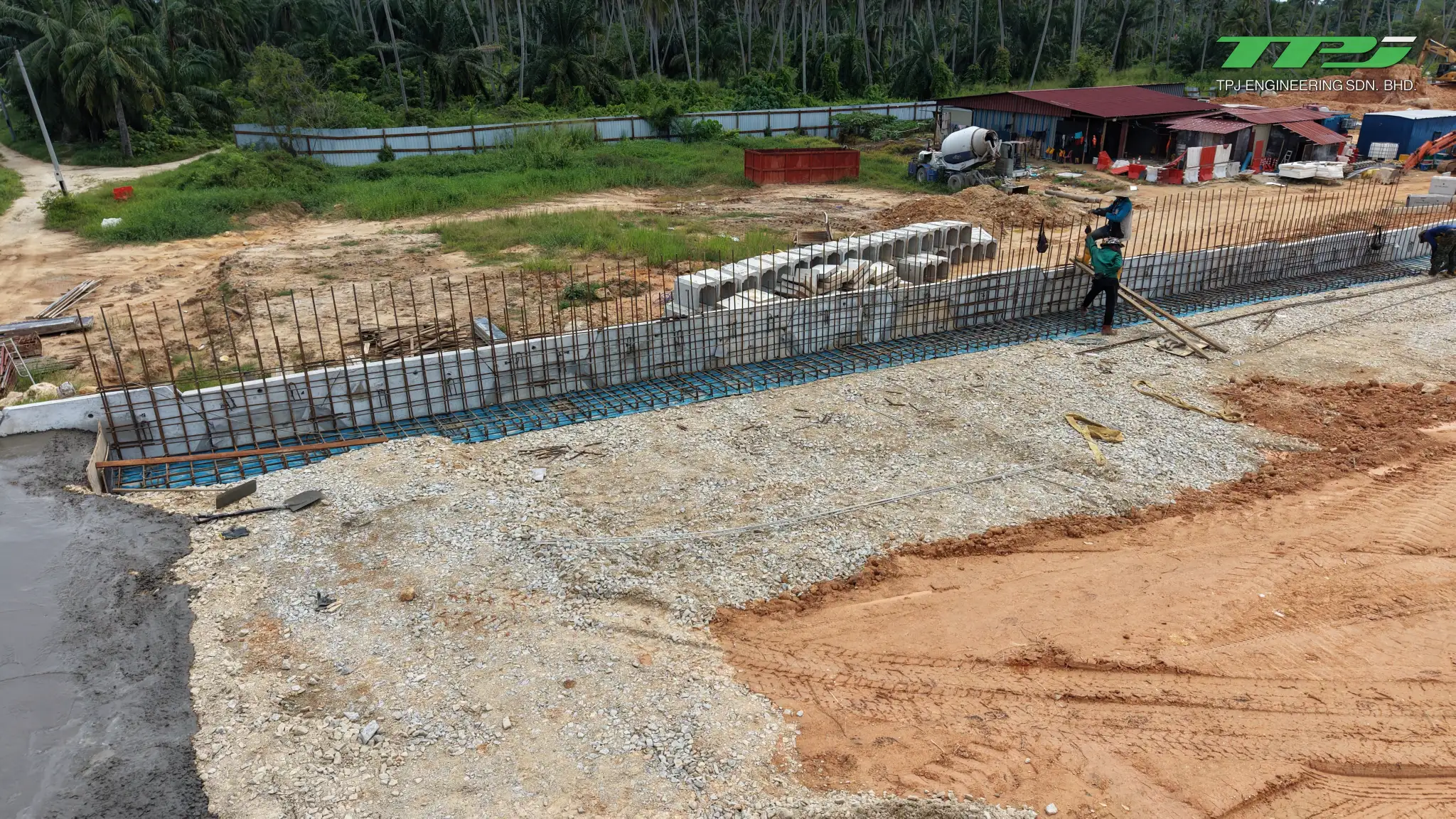 Worker beside exposed reinforcement and concrete panels at the Batu Kawan bridge approach, with drainage units nearby.