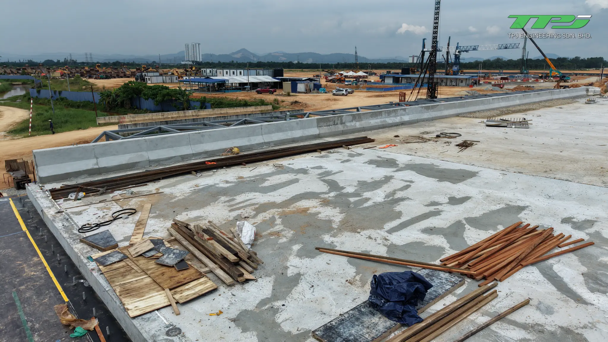 Batu Kawan bridge deck with concrete side barriers, stacked timber and cranes in the background.