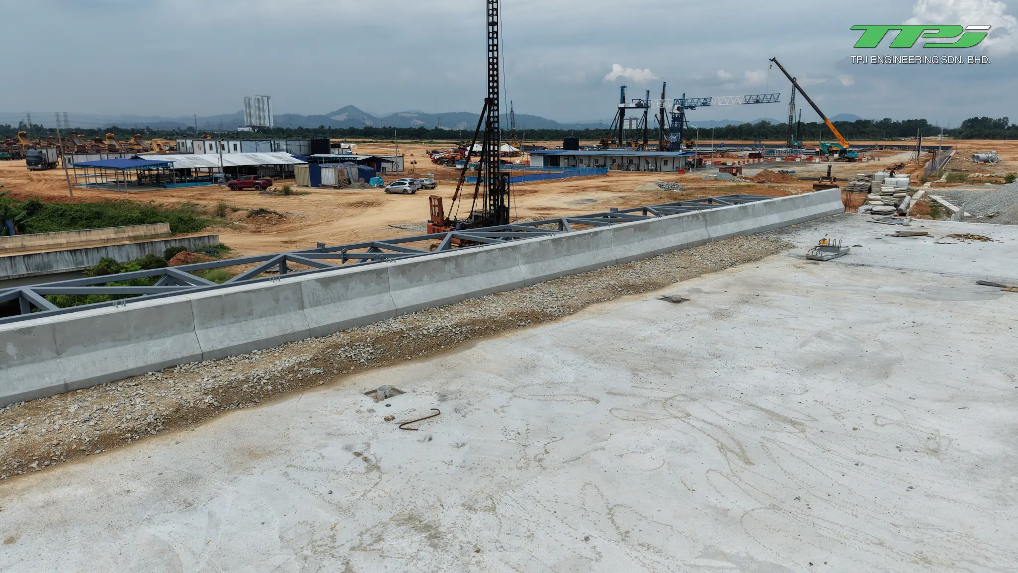 Concrete barrier along the Batu Kawan bridge deck, beside an aggregate strip and construction equipment.