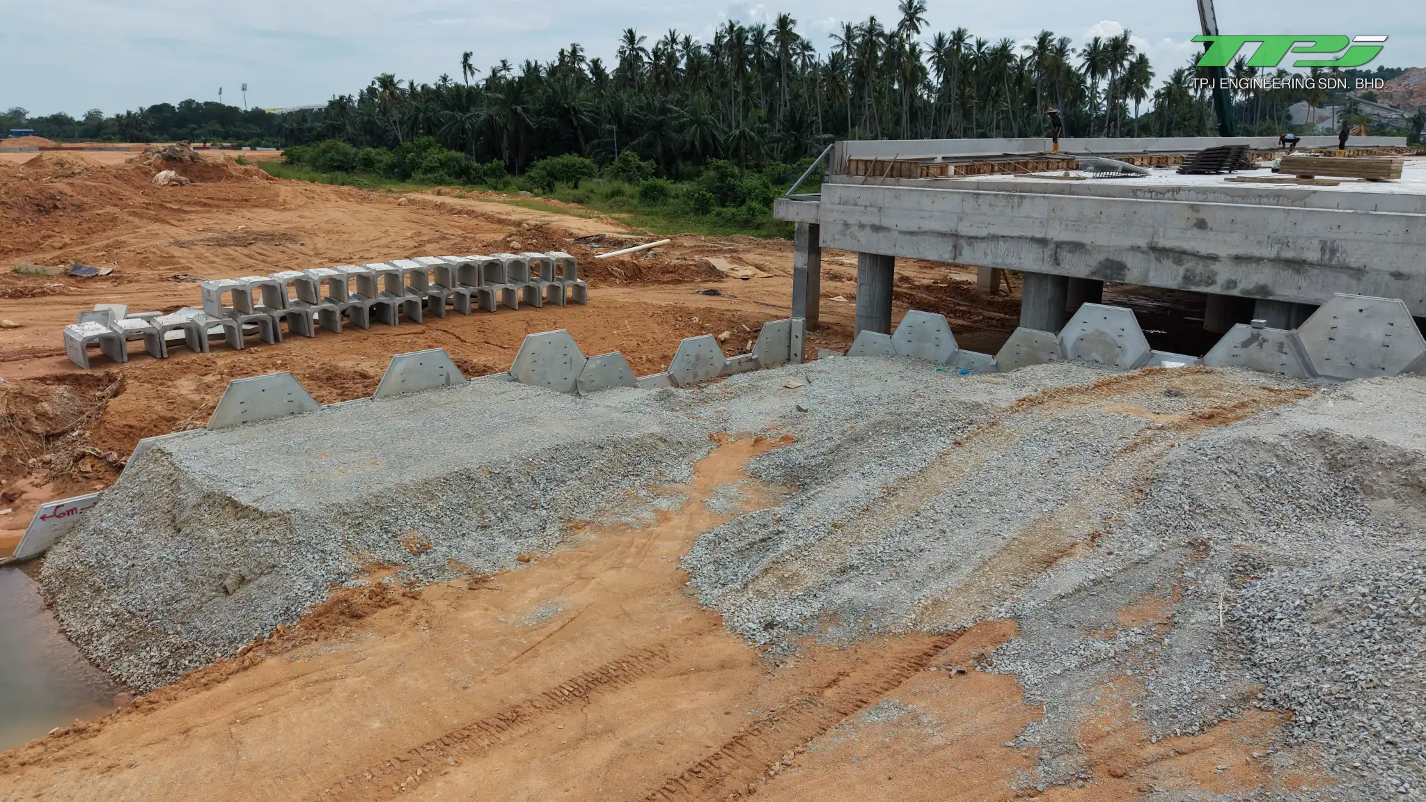 Gravel approach fill, upright concrete retaining panels and stacked drainage units at the Batu Kawan bridge site.